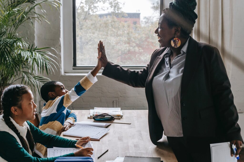 alt="a teacher and young student exchanging a high five."