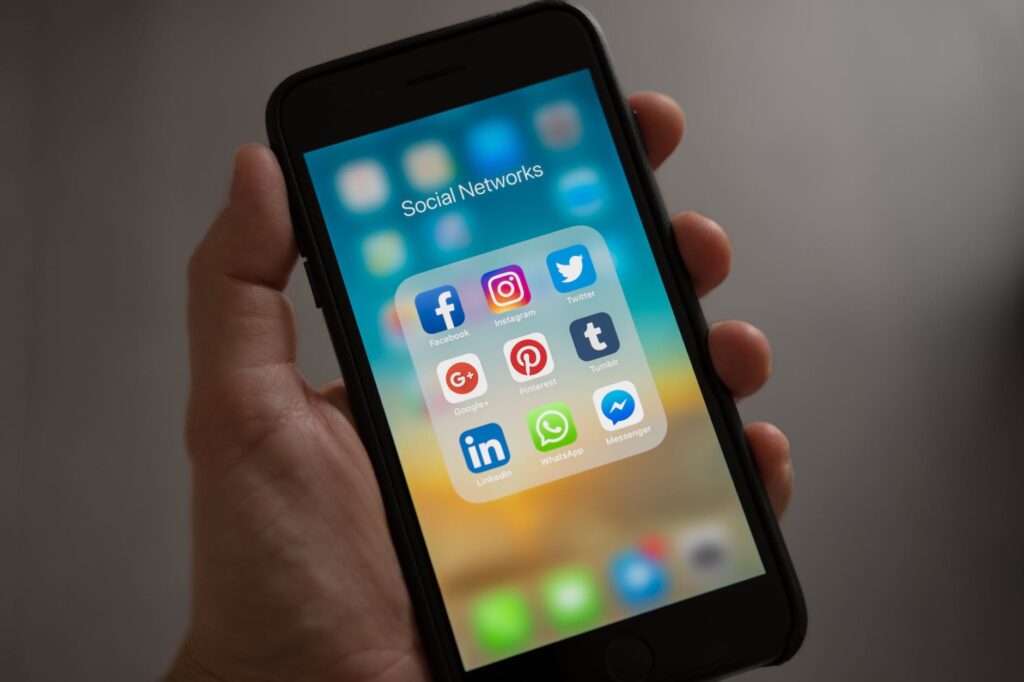 alt="a hand holding a mobile phone with social media icons shown on the screen."