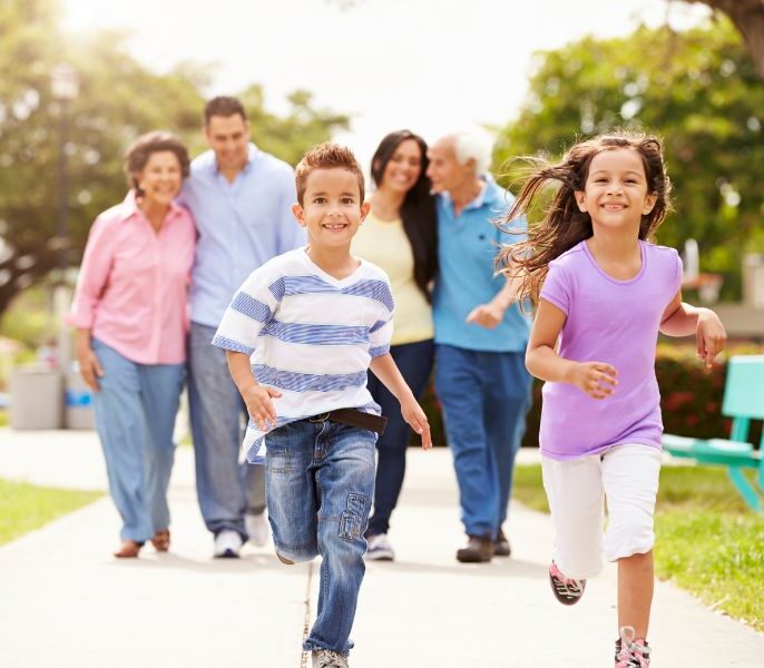 A multigenerational family walking along a path with trees in the background, the two school age children are running ahead in front