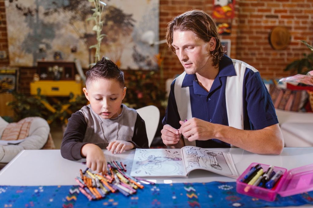 A father and young child sitting at a table with a coloring book and crayons