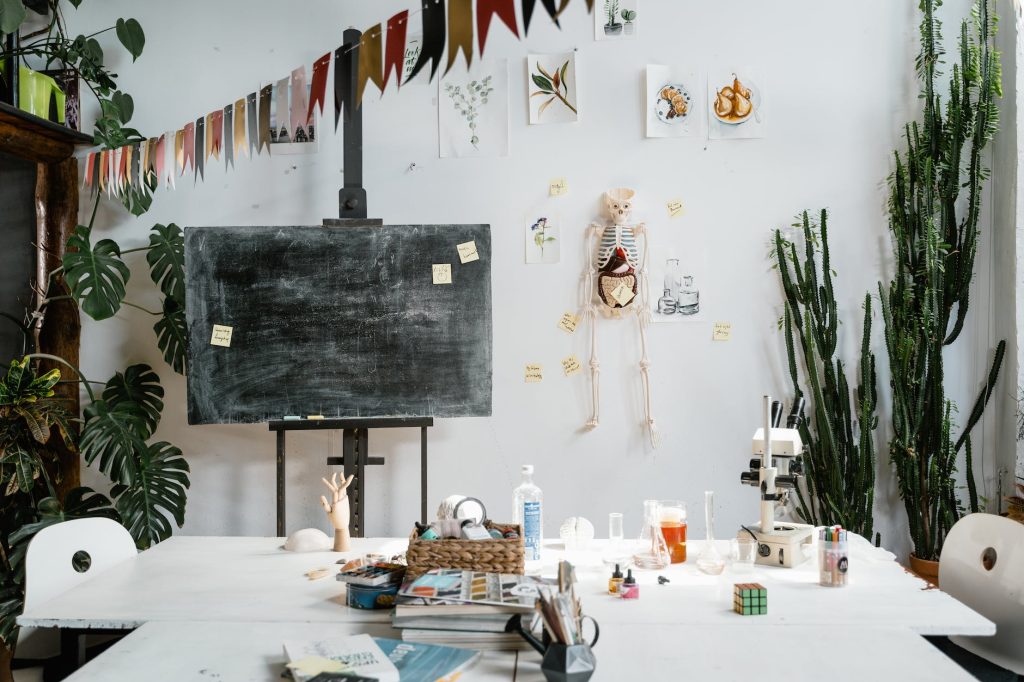 a room with a table, chalkboard and anatomical drawing of a skeleton and organs affixed to the wall