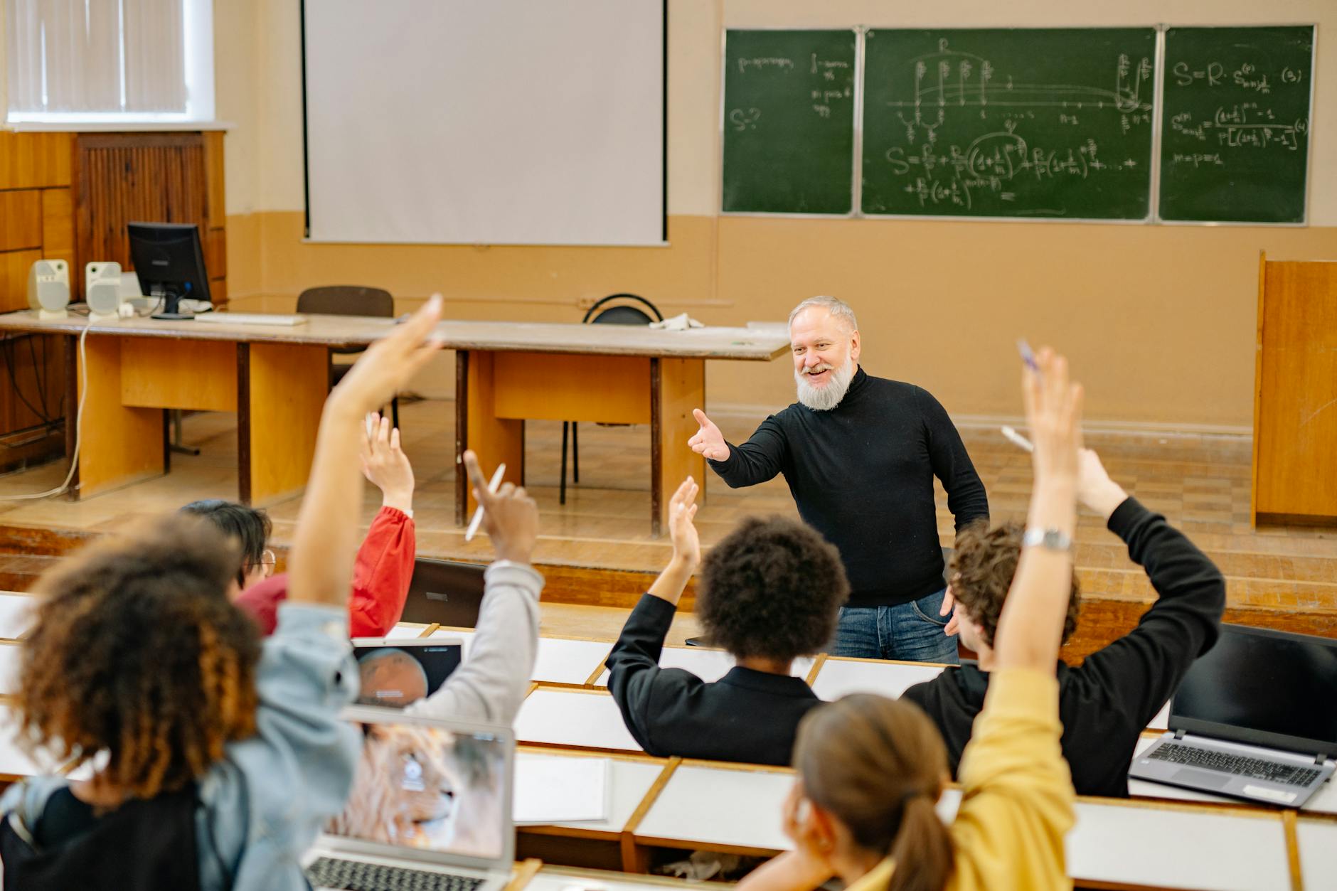 a post-secondary class with an educator in front, the students are raising their hands to answer a question